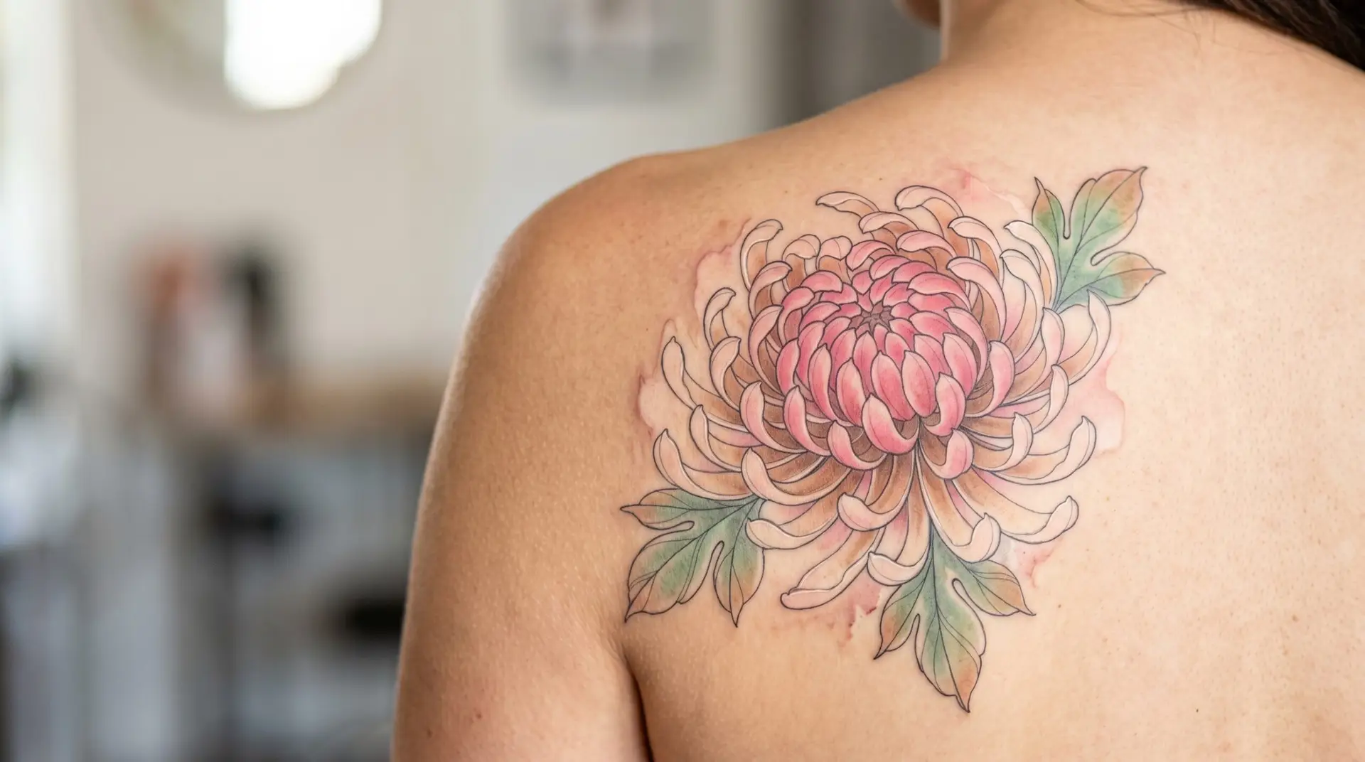 Watercolor pink and bronze chrysanthemum tattoo on shoulder blade with soft color bleed