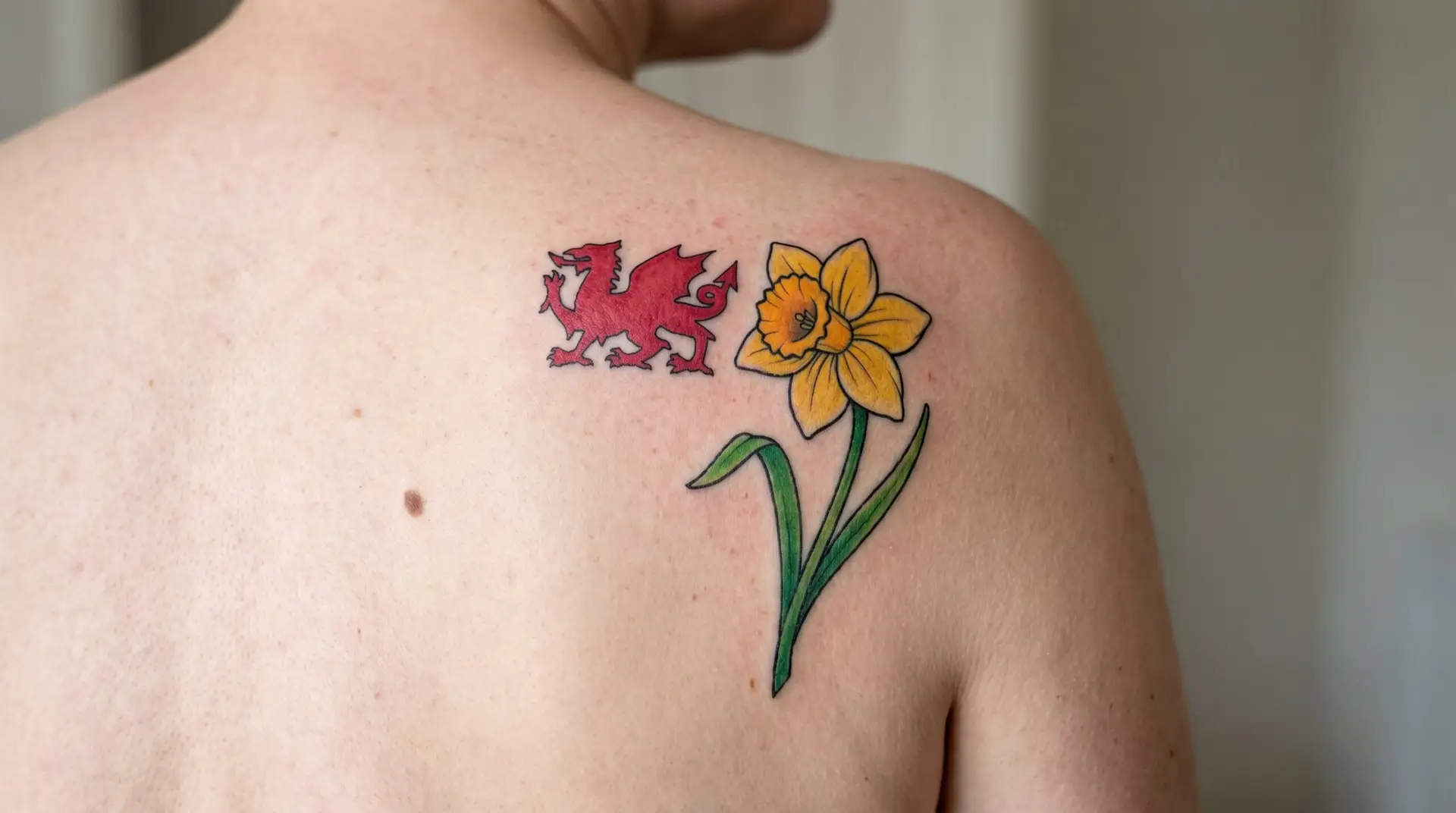 Welsh heritage tattoo with yellow daffodil and small red Welsh dragon silhouette on shoulder