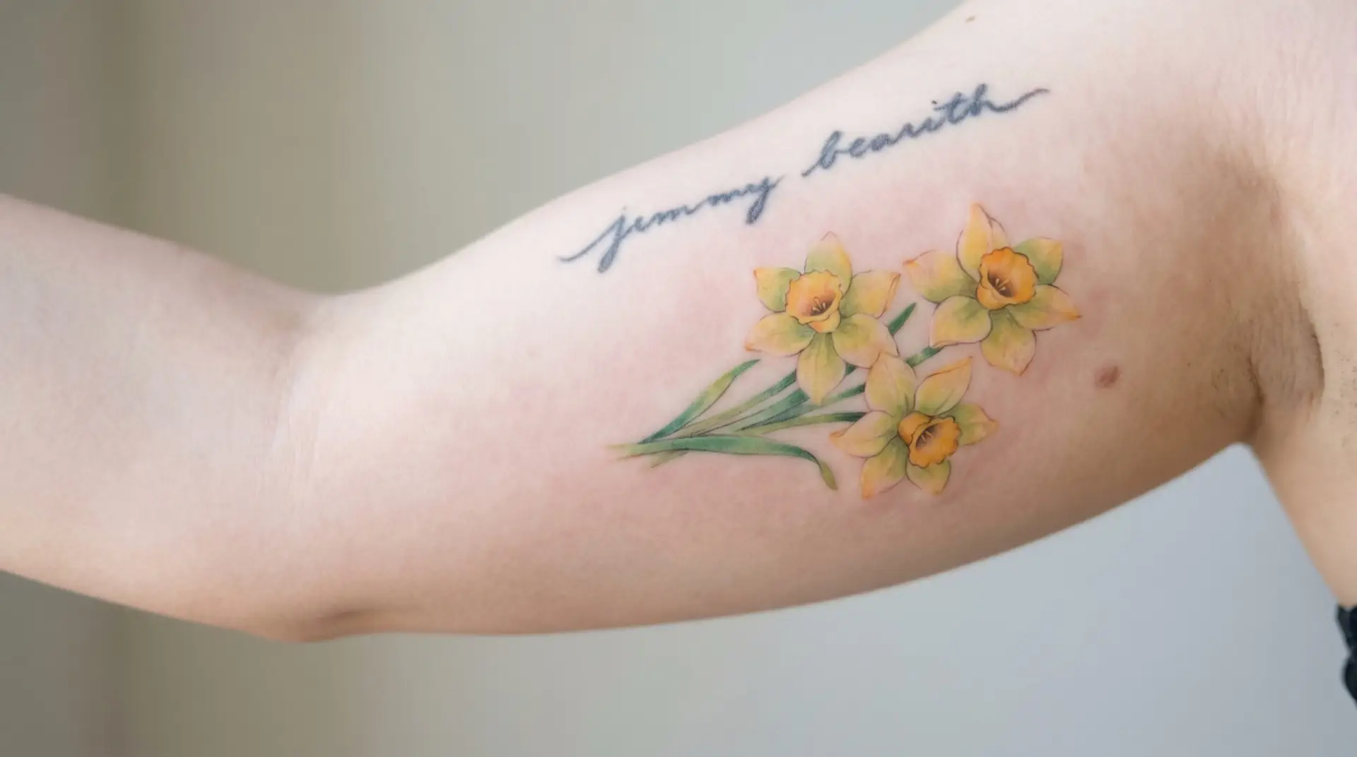 Cluster of three watercolor daffodils on upper arm with cursive Wordsworth quote in dark grey script