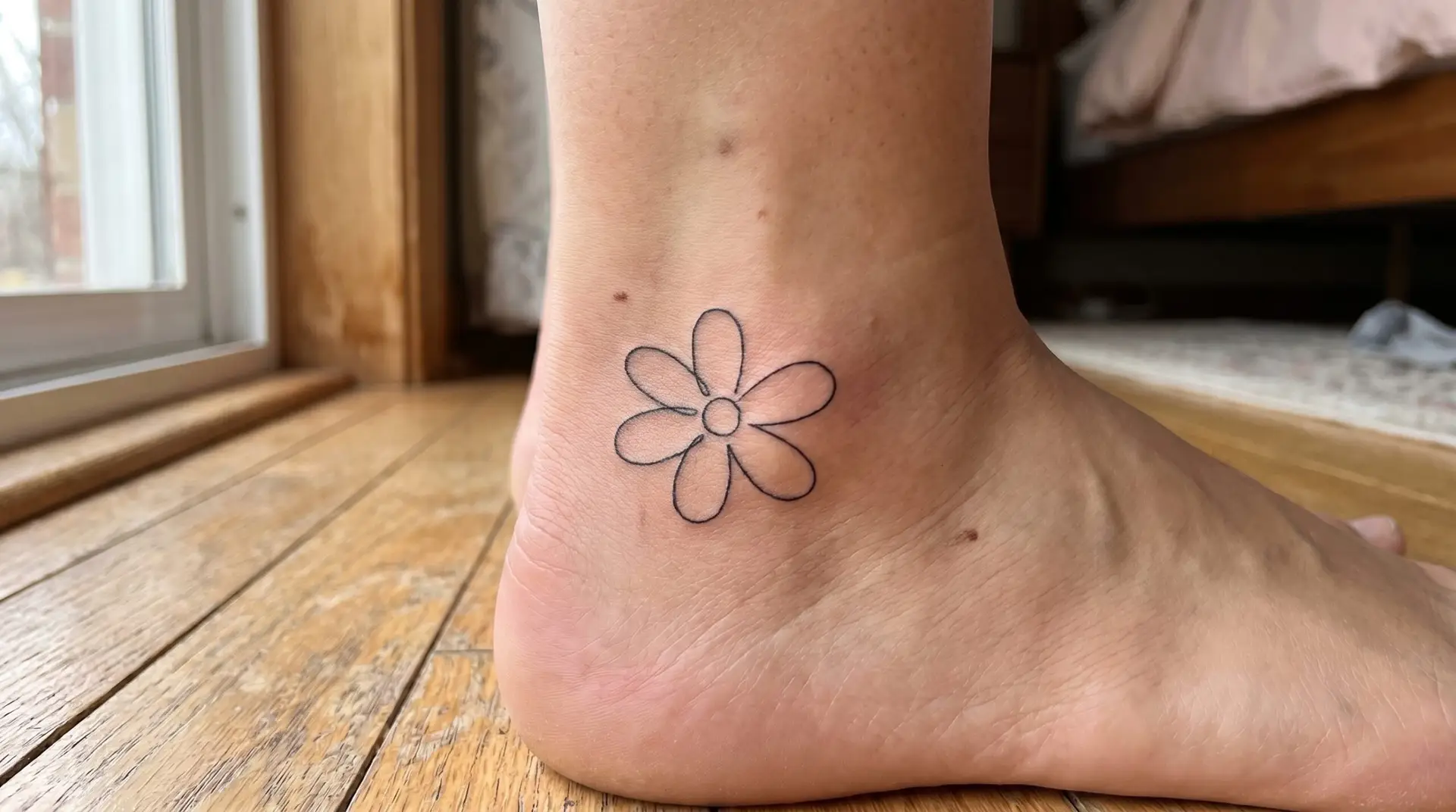 Single-line minimalist daisy tattoo on outer ankle drawn in continuous line in clean black ink