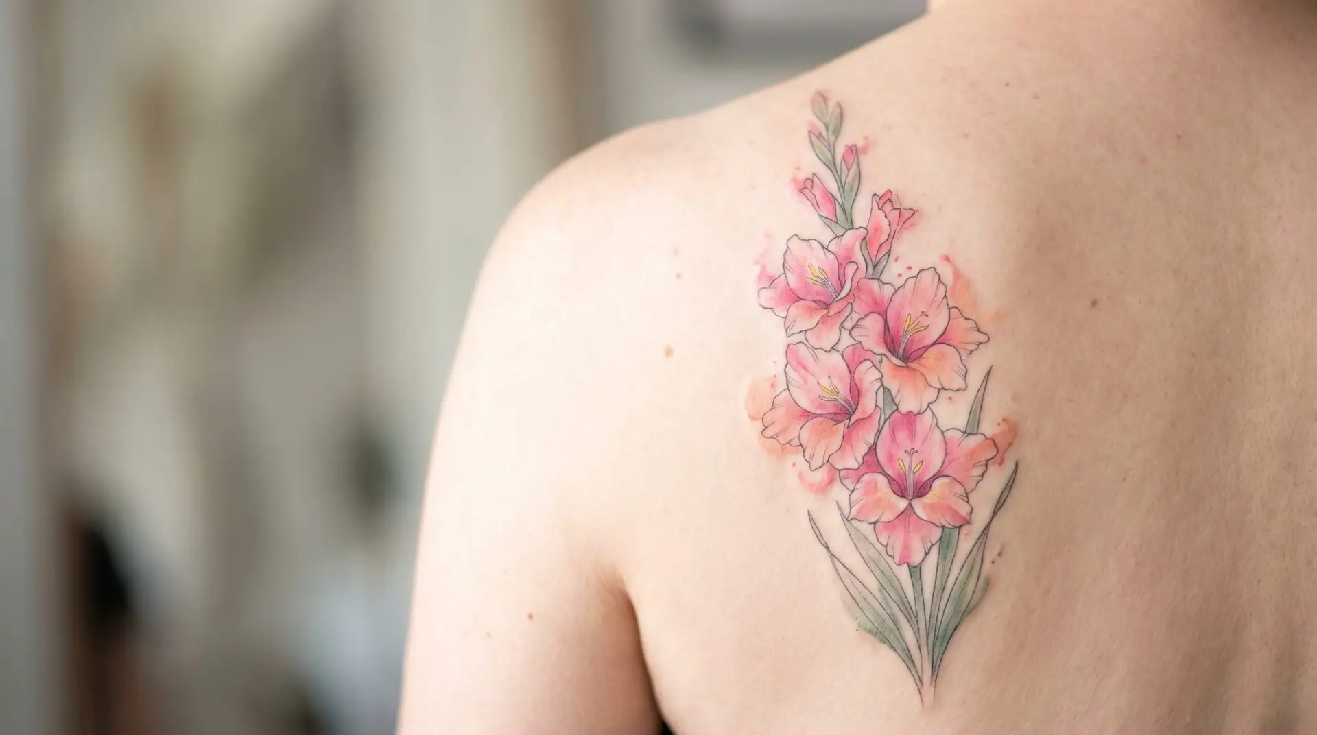 Watercolor pink gladiolus tattoo on shoulder blade with soft salmon color bleed