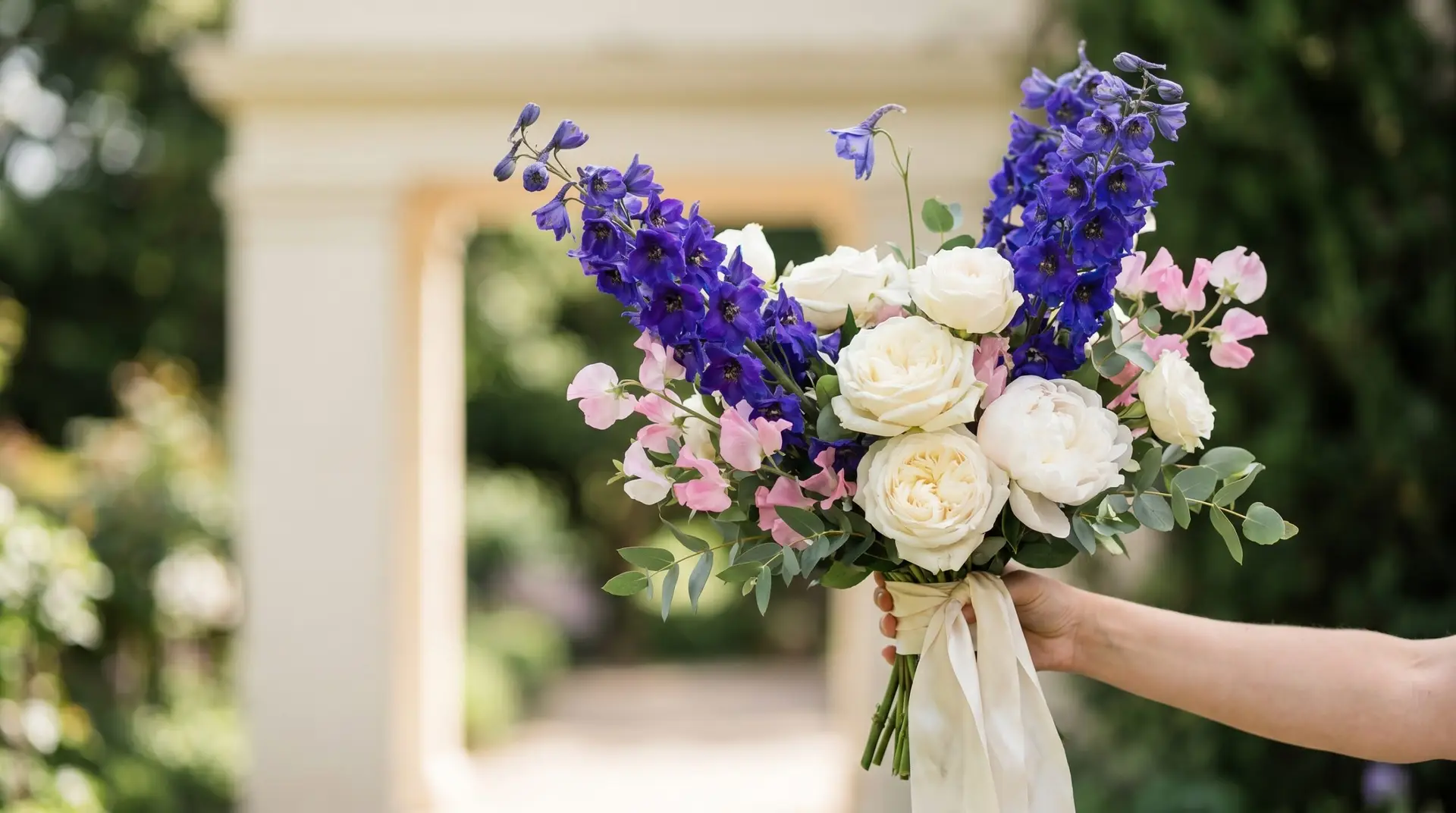 Summer wedding bouquet with deep blue-purple larkspur spires alongside cream roses white peonies