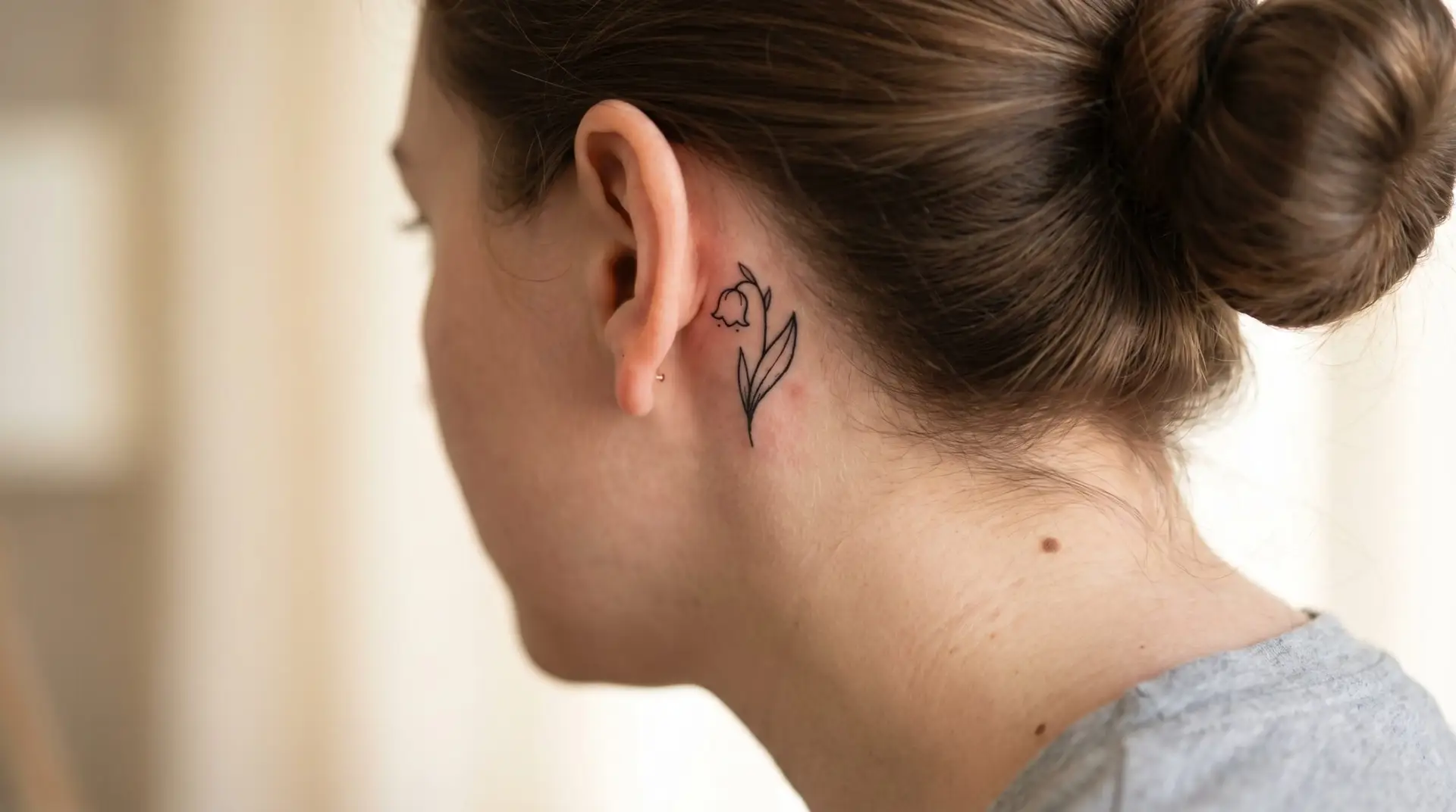Minimalist single lily of the valley bell-flower tattoo behind ear in clean black ink