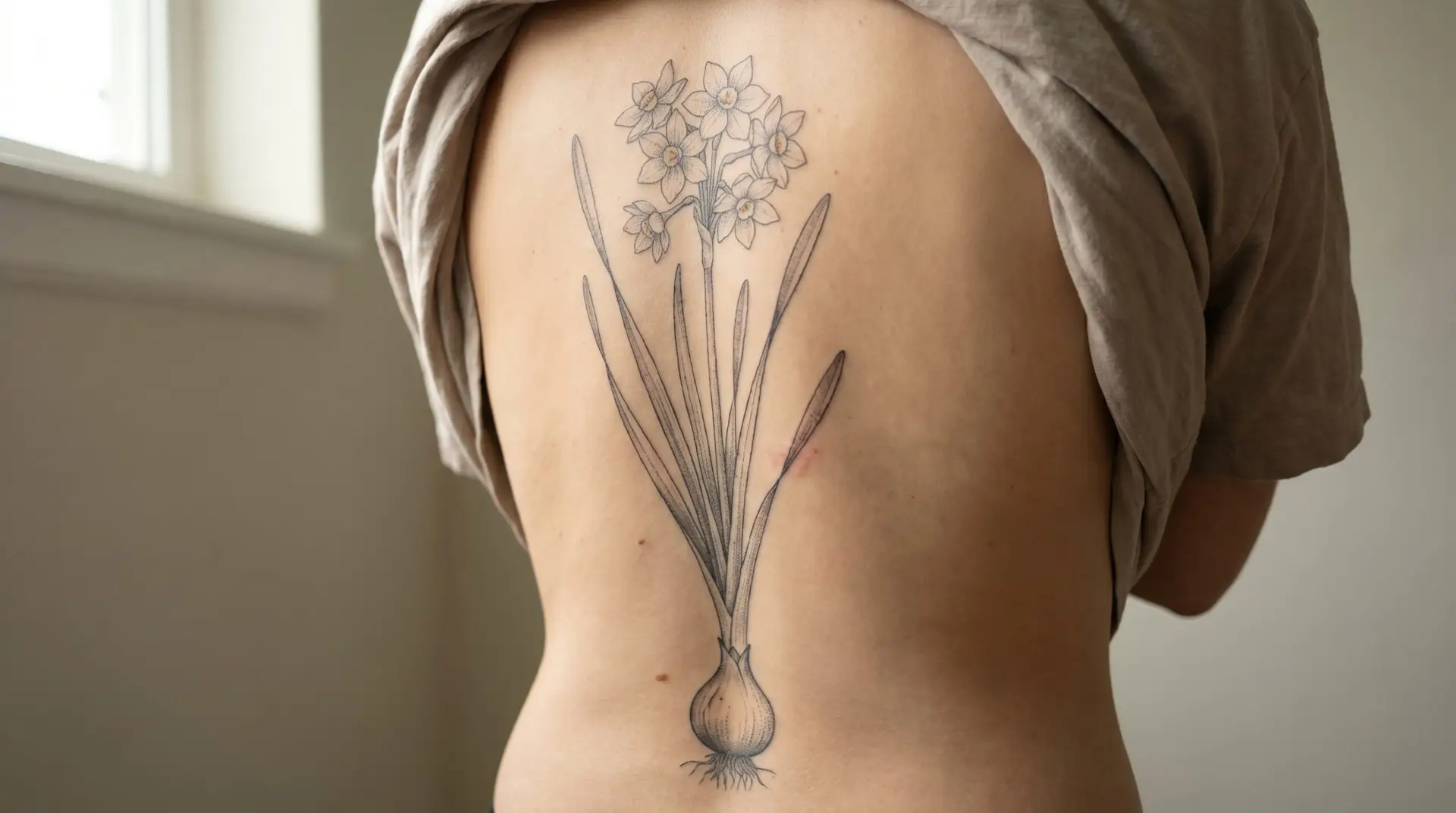 Large botanical illustration narcissus tattoo along spine with full plant bulb leaves and flowers
