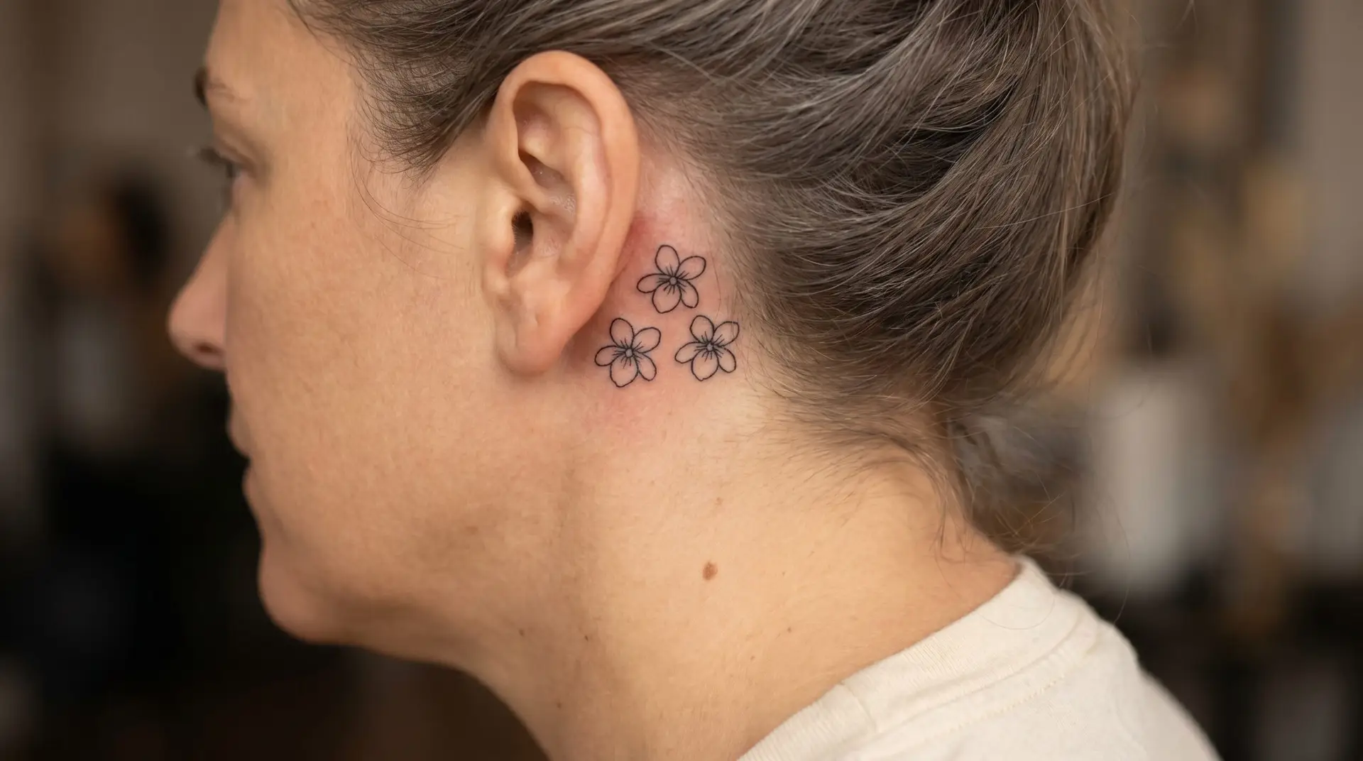 Cluster of three minimalist black violet tattoos behind the ear arranged in small triangular pattern