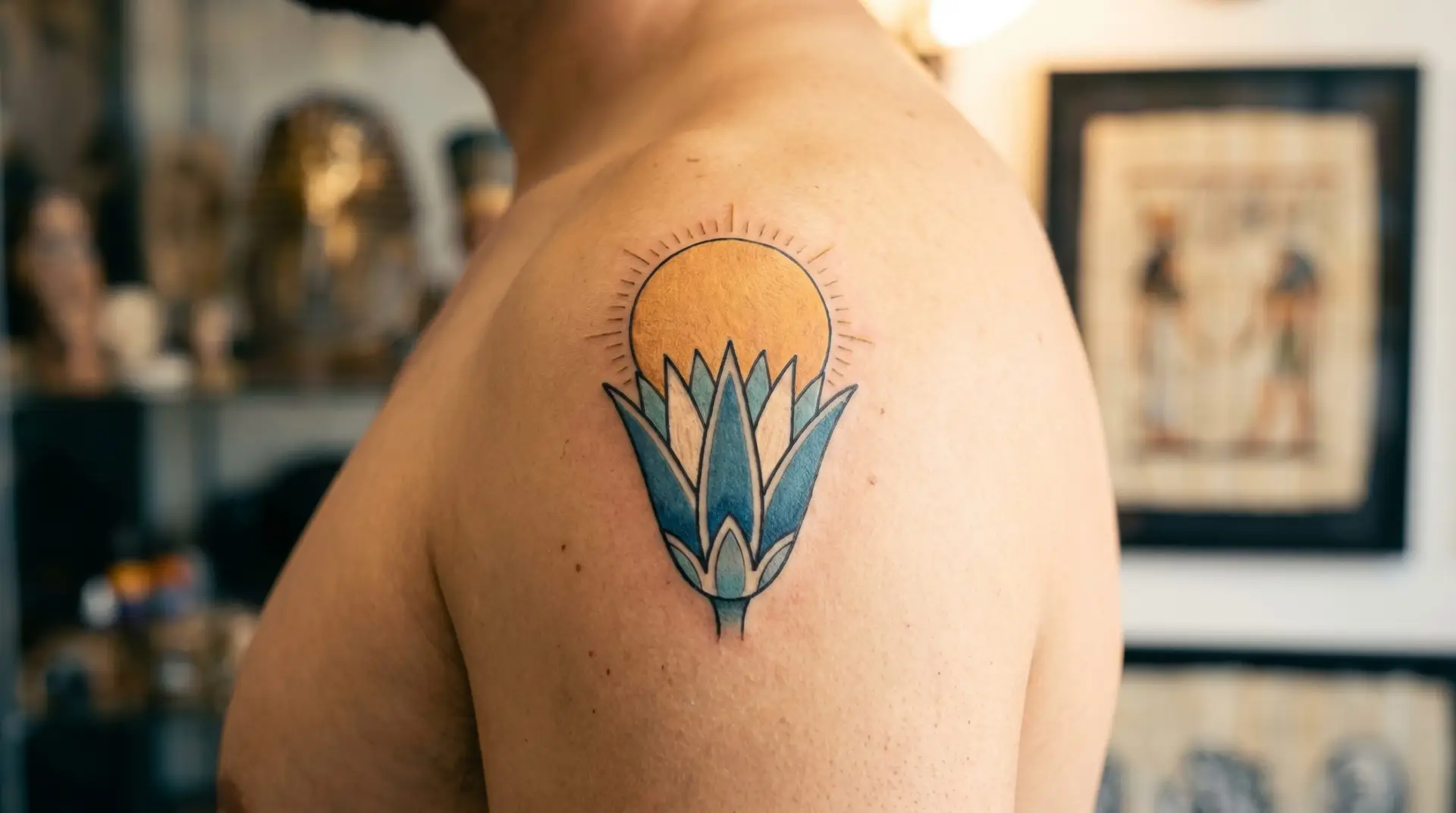 Egyptian-stylized water lily tattoo on shoulder with stylized lotus form and small Egyptian sun disk Ra