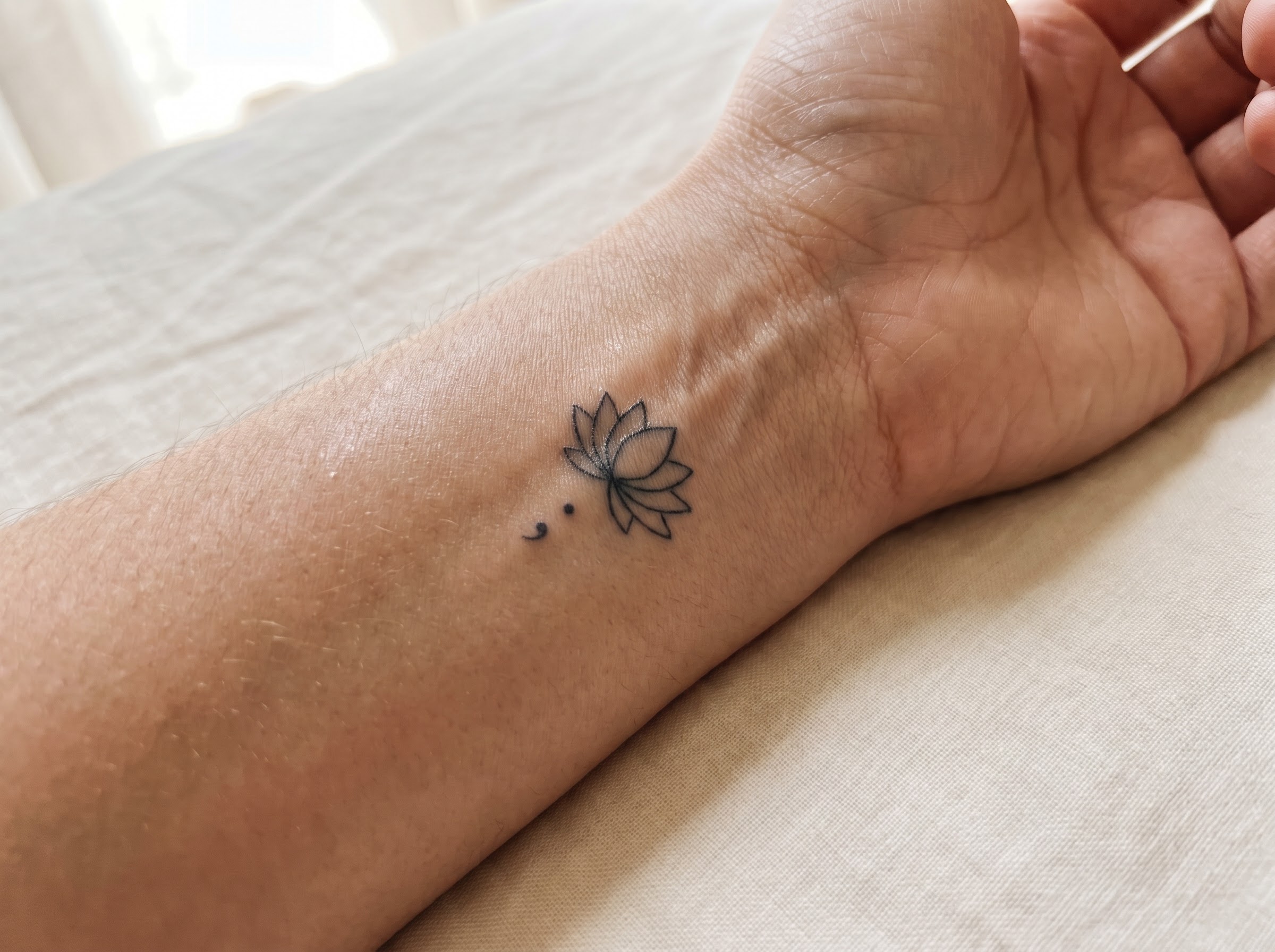 Lotus tattoo paired with a small semicolon on the wrist for resilience and recovery