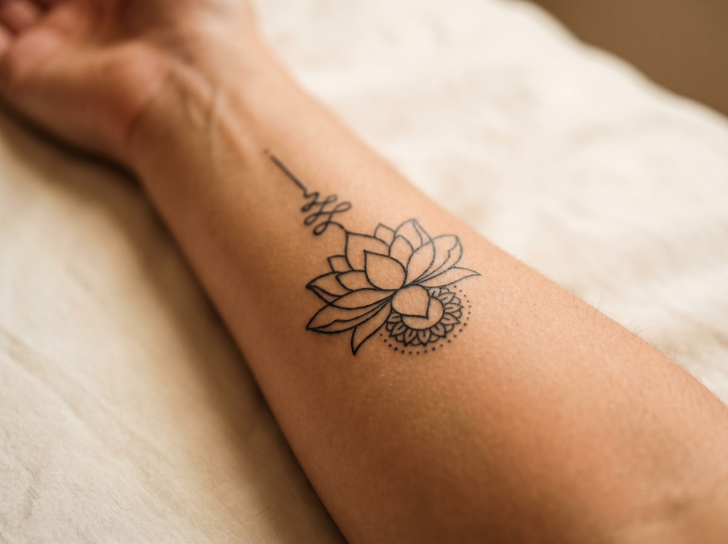 Fine-line lotus tattoo paired with a mandala on skin symbolising resilience and recovery
