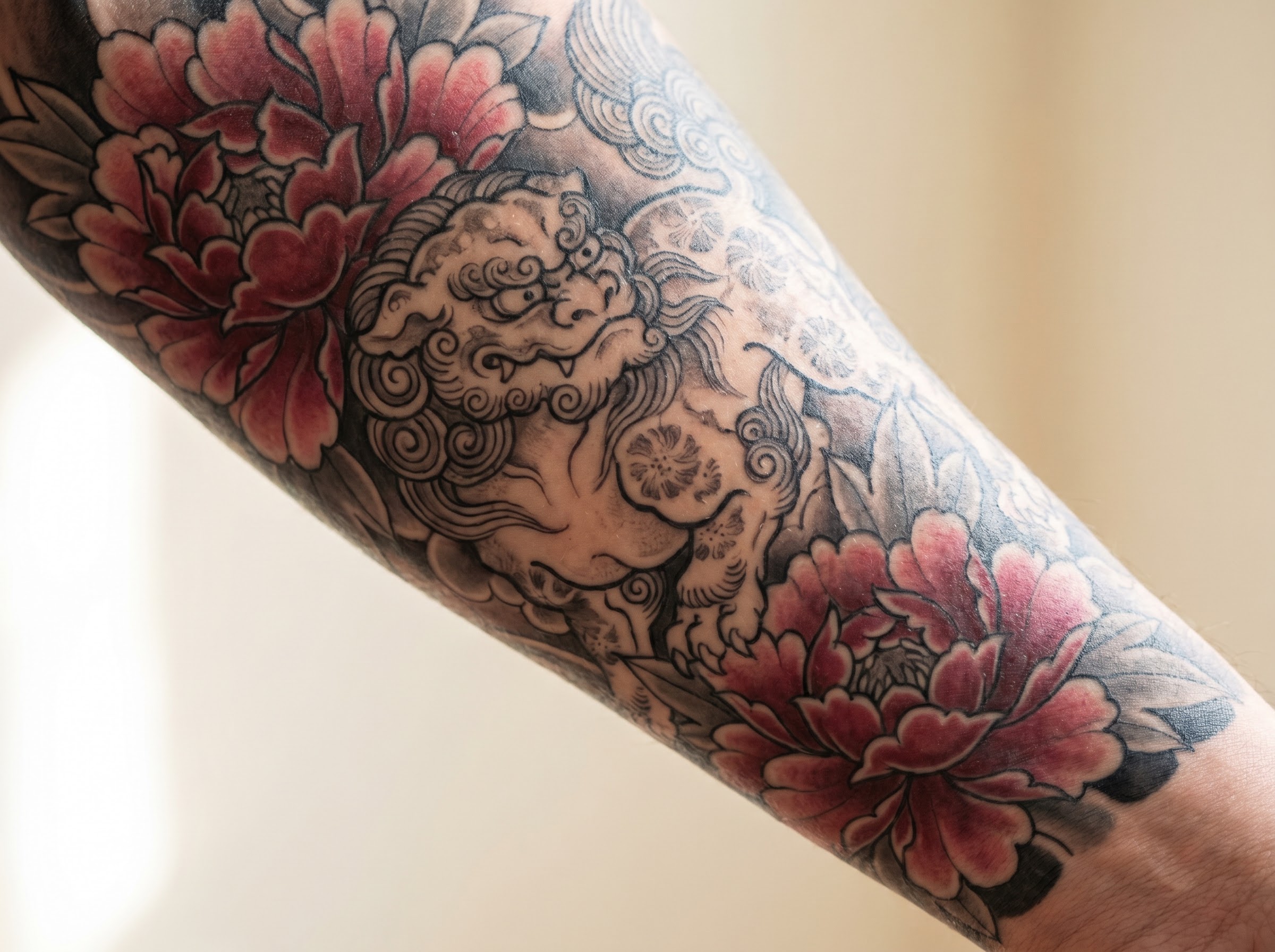Japanese-style peony tattoo paired with a lion-dog guardian reading as bravery and honor
