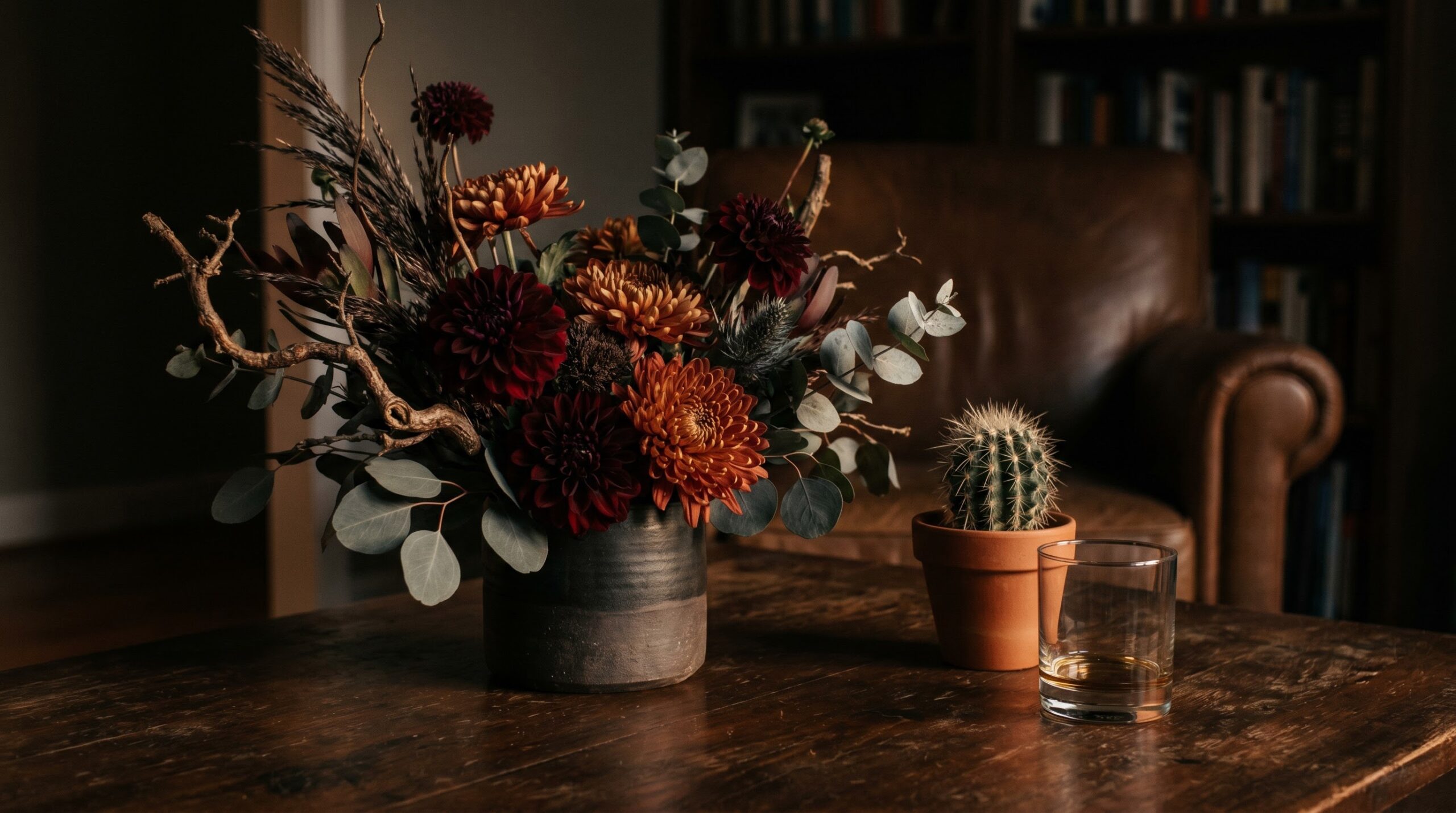 A dark structural arrangement beside a small cactus and a plain glass
