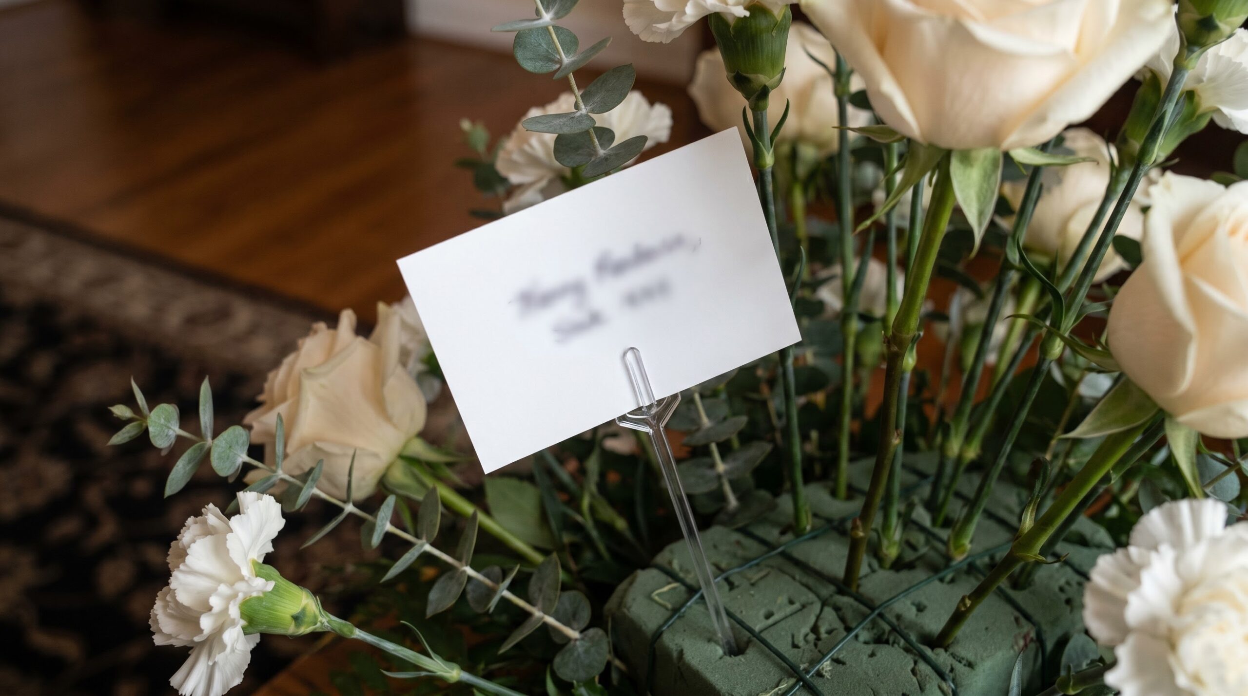 A small white enclosure card tucked into a funeral-home floral standing spray