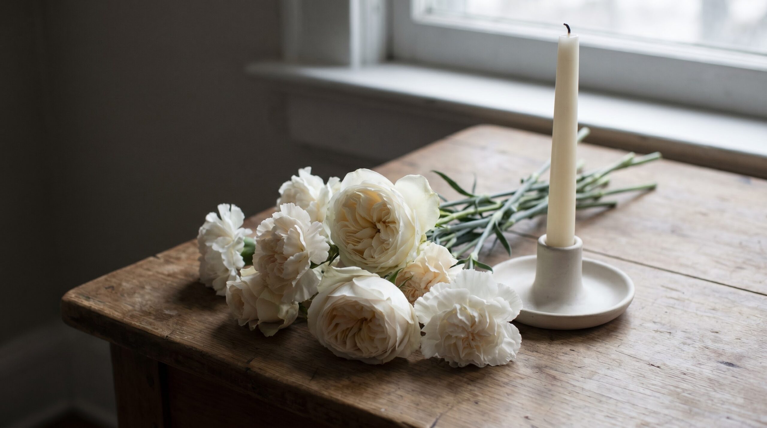 Pale flowers beside an unlit candle on a plain table before a decision