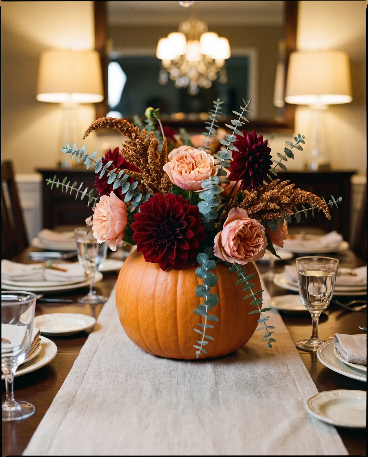 Pumpkin flower centerpiece with dahlias and roses on dining room table.