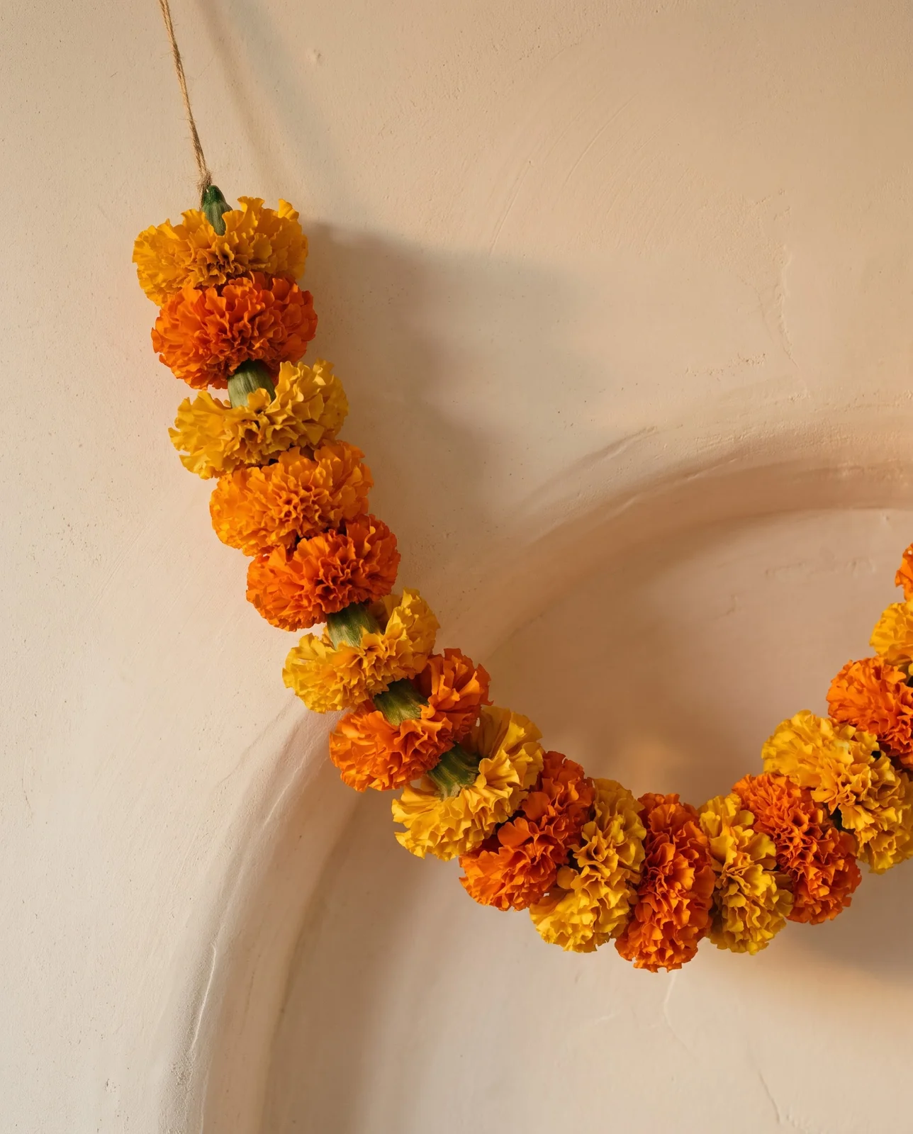Dense orange marigold floral garland hanging against a textured plaster wall.