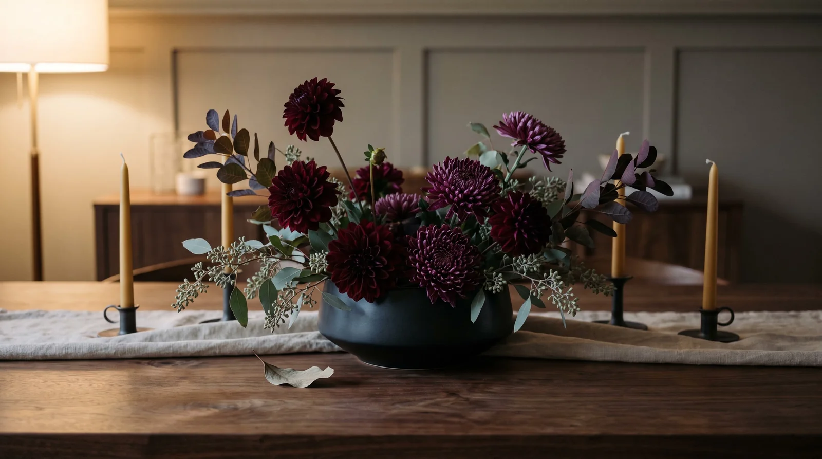 Dark dahlia and mum centerpiece in ceramic bowl on dining table.