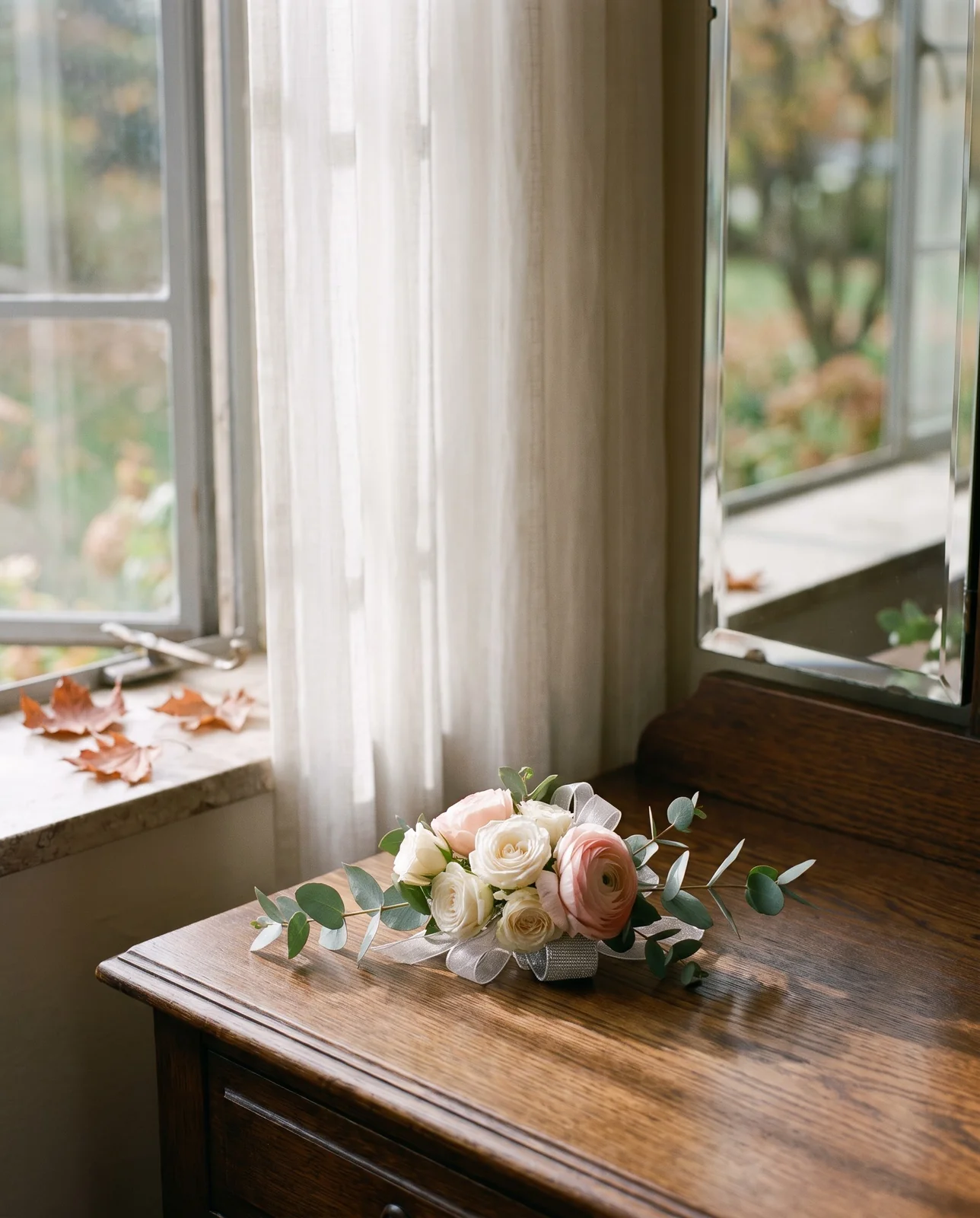 White spray rose and blush ranunculus wrist corsage on wooden vanity table.