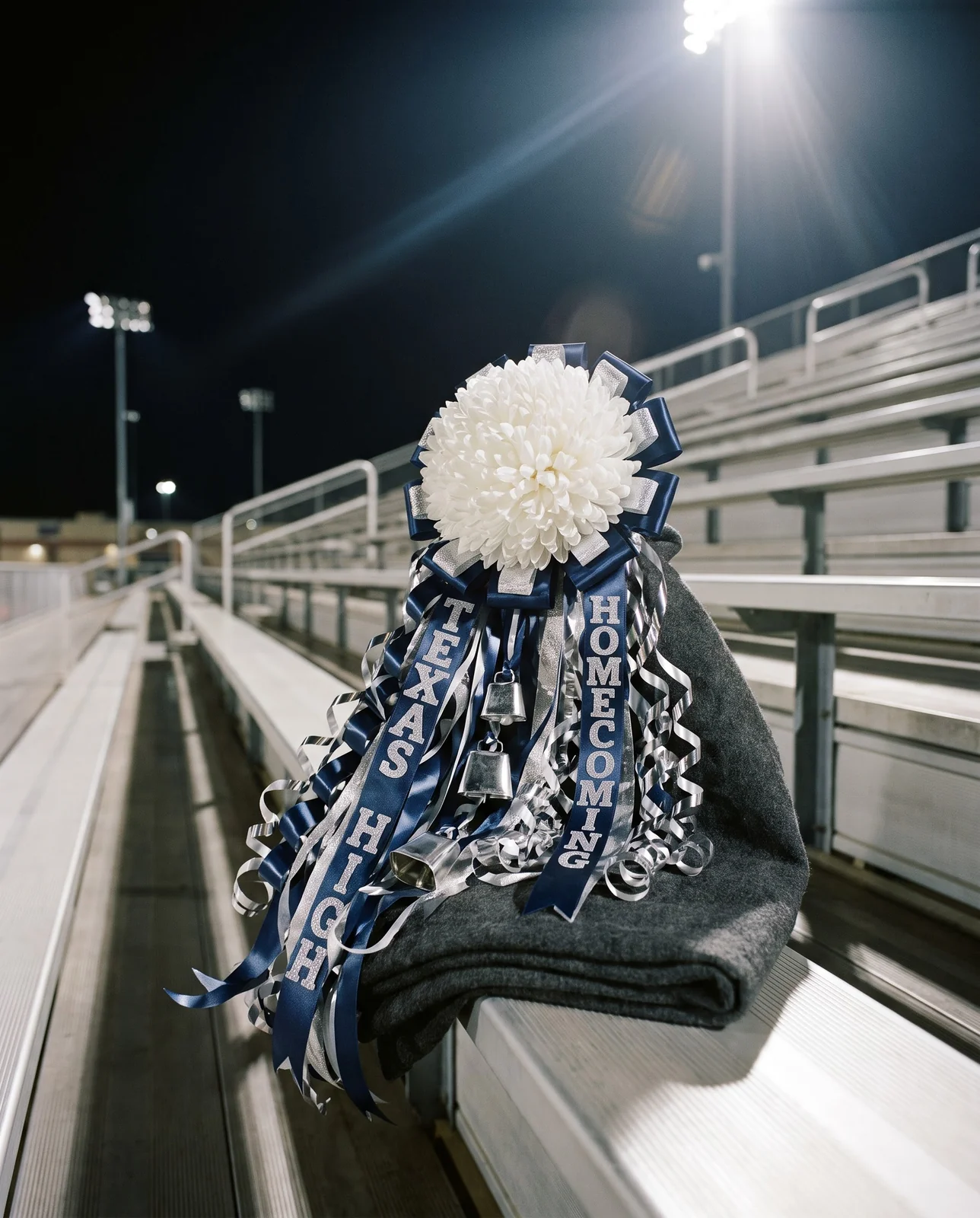 Texas homecoming mum on wool stadium blanket across aluminum bleachers at night.