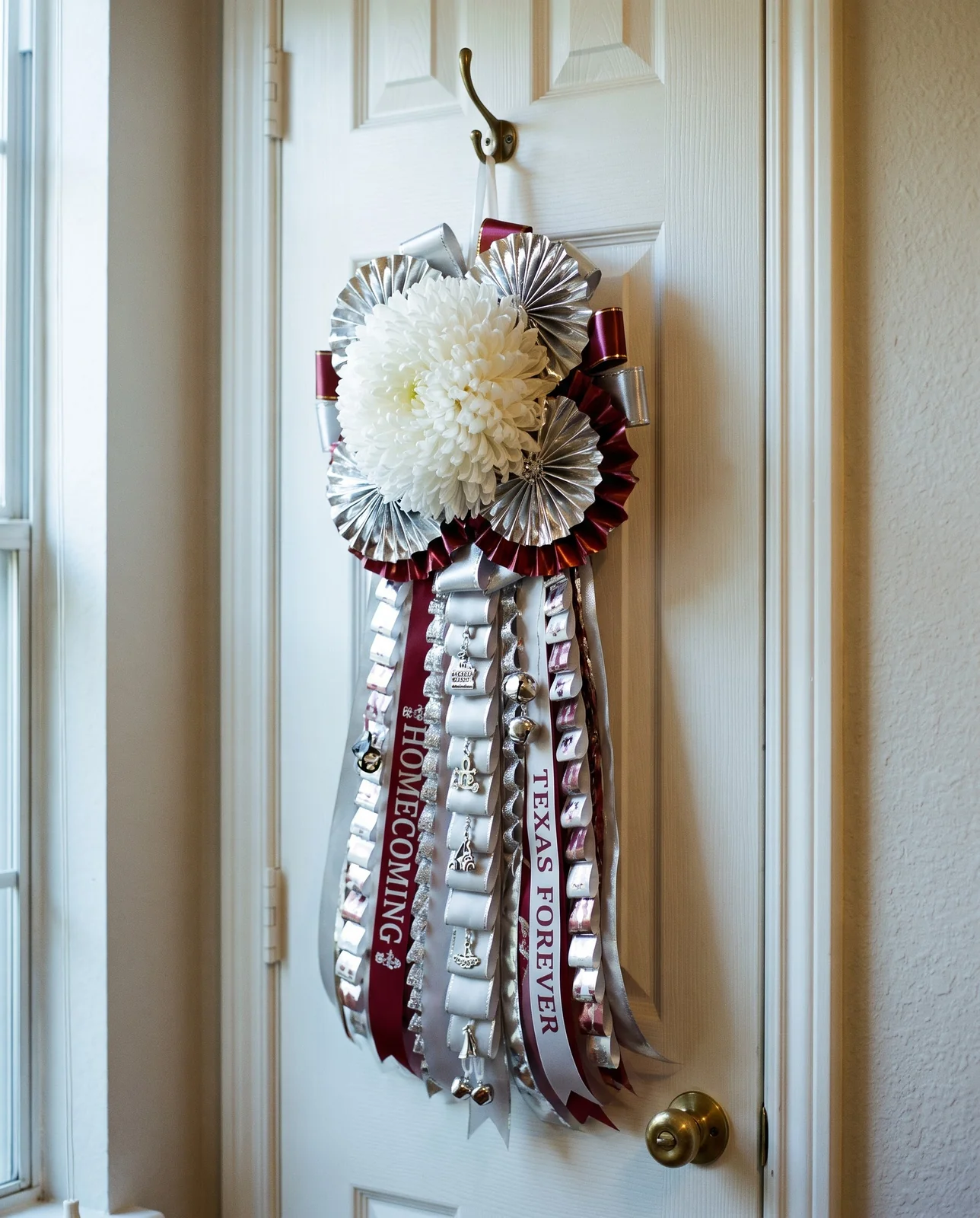 Large Texas homecoming mum with ribbons and bells hanging on closet door.