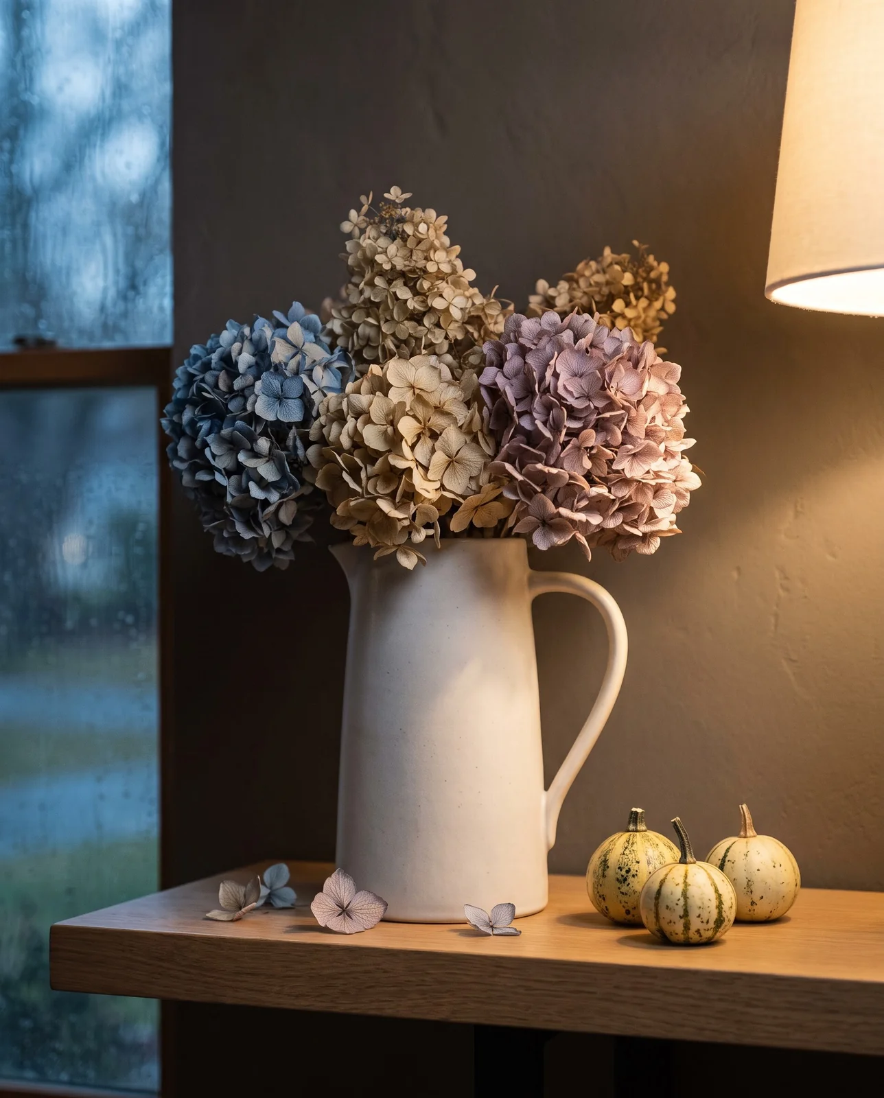 Dried hydrangea arrangement in ceramic vase on high shelf beside small gourds